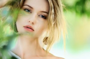 A young woman with beautiful, full lips, pulls her hair back from her face.