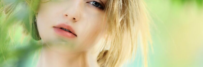 A young woman with beautiful, full lips, pulls her hair back from her face.